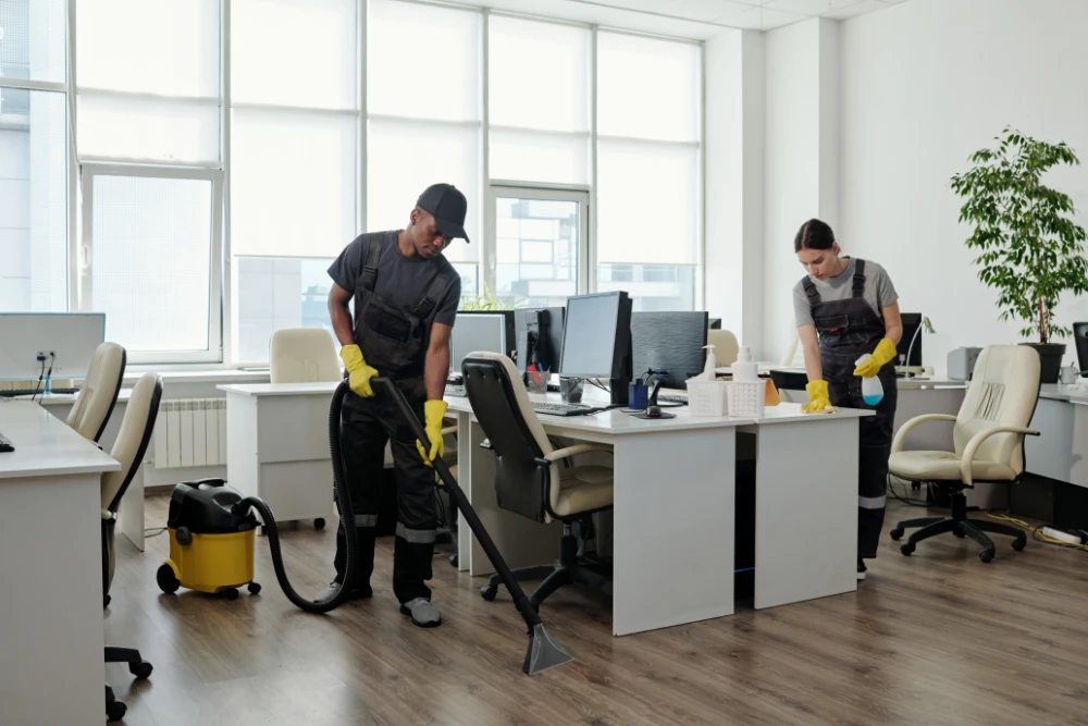 young-black-man-workwear-cleaning-floor-while-girl-wiping-desks-with-computers